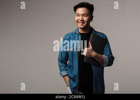 Image of cheerful handsome asian man smiling and holding laptop isolated over gray background Stock Photo