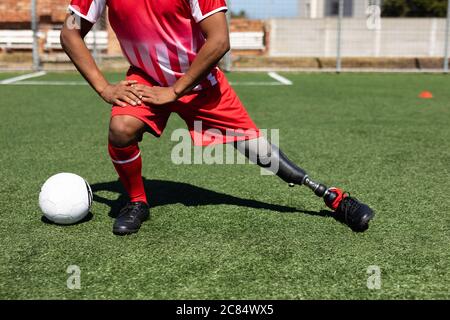 Low section of mixed race male football player with prosthetic leg wearing a team strip training at a sports field in the sun, warming up stretching l Stock Photo