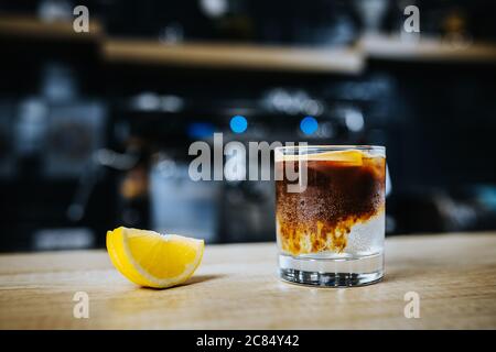 A slice of lemon next to a glass of iced coffee - a dense liquid flows into the bottom layer of the cocktail Stock Photo