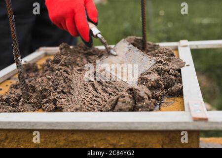 Hands of a professional bricklayer with gloves while working on the construction of stone walls - a trowel for applying masonry mortar and a mallet fo Stock Photo