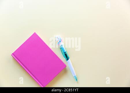 Pink notebook for notes, funny unicorn pen on yellow pastel background. Flat lay. Top view. Copy space Stock Photo