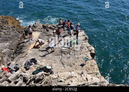 Cascais, Portugal - June 7, 2017: Local fishermen with fishing rods catch fish from the rocky shore Stock Photo