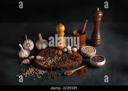 Still life with different kind of spices like pepper, nutmeg, garlic, cinnamon, and paprika on a black background. Stock Photo