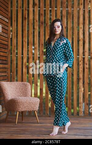 Woman standing in pajamas pajamas with polka dots on wooden background in full length. Caucasian female model. Stock Photo