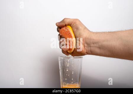 Male strong hand squeezes juice from a ripe grapefruit into a glass. Fruit citrus juice. Stock Photo