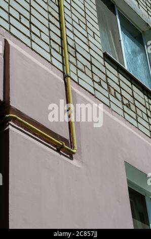 Yellow gas pipe viewed on the outer brick wall of residential building. Facade of multi-storey apartments with gas pipeline. Partial thermal insulatio Stock Photo