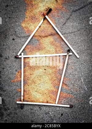 Matchstick house on concrete background with flames coming out Stock Photo