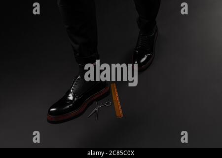 On a black dusty surface are old barber tools. Vintage manual hair clipper comb and scissors under flying leather shoes Stock Photo