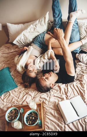 Upper view photo of a caucasian couple lying in bed and embracing before eating cereals with milk Stock Photo