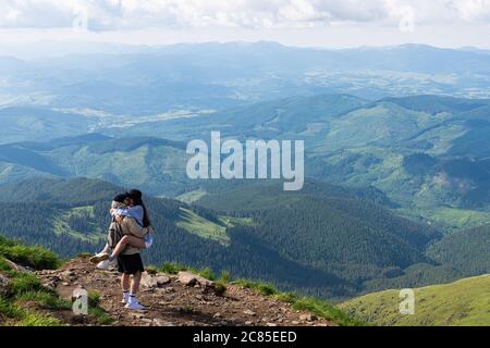Loving couple of tourists with backpacks in the hike kiss on the top in the mountains Stock Photo