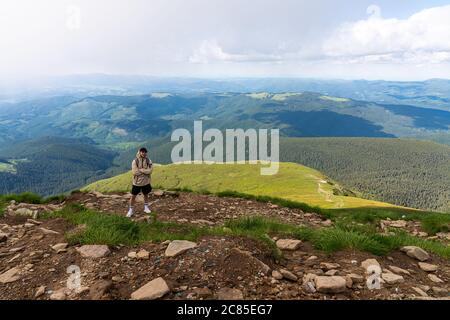Mountaineer with backpack on rock enjoying view of big mountains, hiking lifestyle, man on top Stock Photo