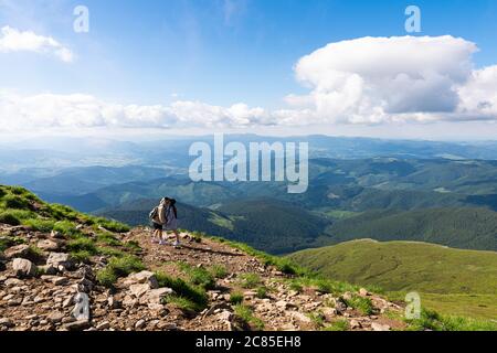 Young couple with backpacks traveling together in mountains. Happy hipster man kissing his girlfriend on the top Stock Photo
