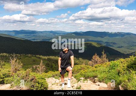 An european young man, standing on the top of the mountain, facing the sun, meditating and thinking about the sense of life, grieving Stock Photo