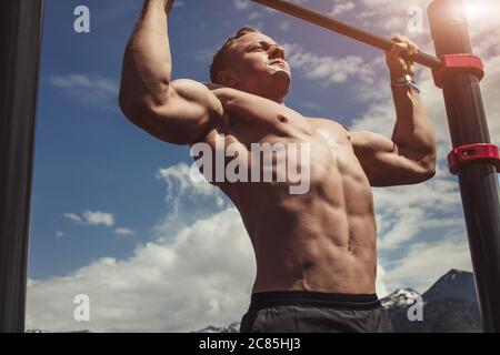 Caucasian male athlete with fit torso and strong hands doing chin ups outdoor. Handsome blonde sportsman pulls up on stadium horizontal bar. Chin up b Stock Photo Alamy