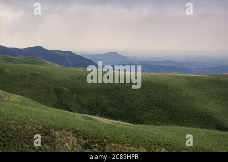 of the grass covered sloped of the Drakensberg mountains , South Africa, with rain in the distance Stock Photo