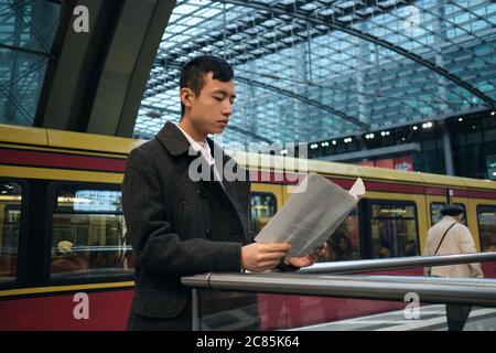Young Asian businessman confidently reading newspaper at city subway station Stock Photo