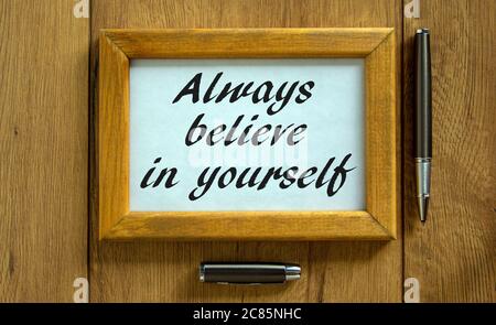 Wooden picture frame with inscription 'always believe in yourself' on beautiful wooden background. Pen and cap on the table. Concept. Stock Photo