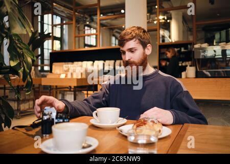 Young handsome bearded man having coffee break in cafe Stock Photo