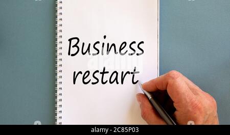 Male hand writing ' business restart' on white note, isolated on blue background. Stock Photo