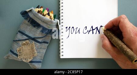 Hand writing 'you can', isolated on blue background. Bunch of pencils stylized tree branch in bag. Stock Photo