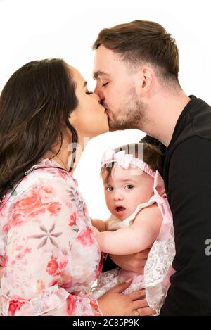 Vertical lifestyle portrait of a young couple kissing with their daughter's amazed expression on her face. Stock Photo