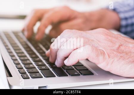 Older person's hands typing on a gray laptop. Selective focus. Stock Photo