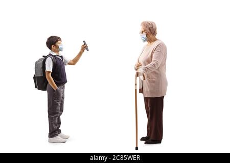 Full length profile shot of a schoolboy wearing a protective face mask and showing mobile phone to an elderly woman isolated on white background Stock Photo