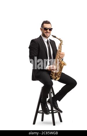 Full length portrait of a man sitting on a chair with a saxophone and smiling at the camera isolated on white background Stock Photo