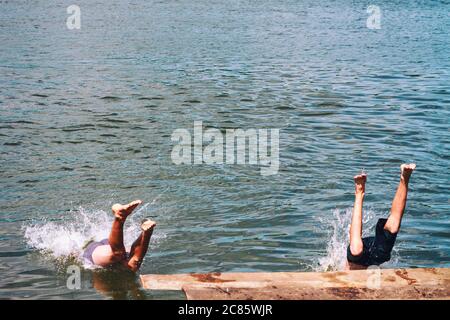 men jumping off wooden pier, feet splashing on entry to water Stock Photo