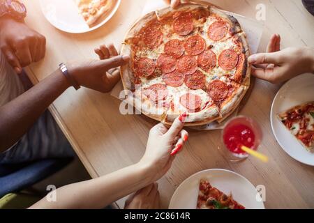 Human hands close up grabbing pizza slices from wooden background. Stock Photo