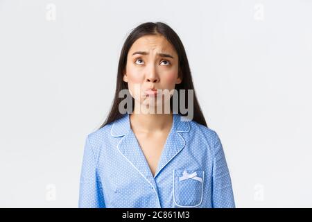 Close-up shot of miserable and sad cute asian girl in pajama sulking, pouting and whining as looking up with jealousy, feeling regret or Stock Photo