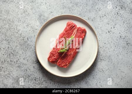 Raw ribeye steak with rosemary on grey. Stock Photo