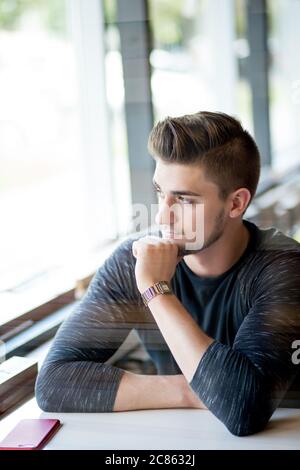 Caucasian man with stylish haircut looking pensively at the window while waiting for his girlfriend at cafe. Stock Photo