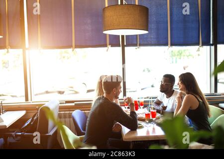 Hungry multiethnic male and female co-workers having lunch break together eating pizza in corporative diner, discussing working projects. Stock Photo