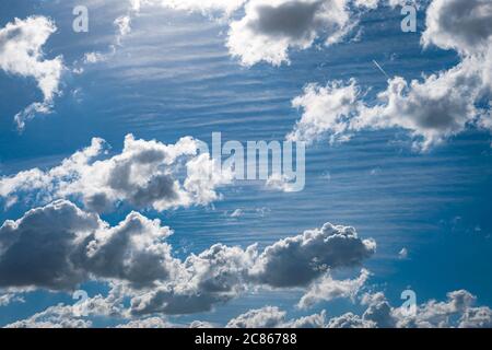 Cumulus clouds on a sunny summer day. At a higher level in the atmosphere striped cirrus clouds can be seen. Suitable as background or wallpaper. Stock Photo