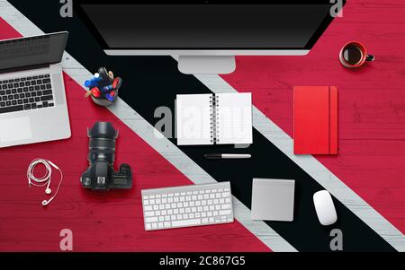 Trinidad And Tobago flag background with headphone,camera, notebook and mouse on national office desk table.Top view with copy space.Flat Lay. Stock Photo