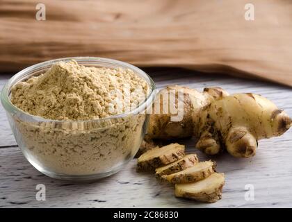 Ginger powder in glass bowl on wooden board with ginger roots and slices. Healthy eating concept. Stock Photo