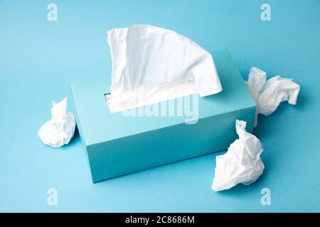 Light blue tissue box and crumpled tissues on blue background. Cold and flu concept. Minimal monochromatic composition. Stock Photo
