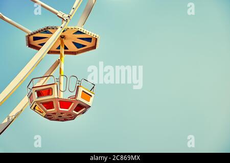 Retro toned close up picture of Ferris wheel car with cloudless sky in background, space for text. Stock Photo