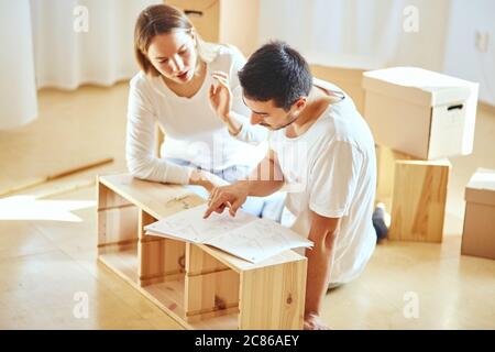 couple reads instructions for Assembly of furniture in new house with moving boxes on background Stock Photo