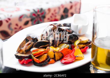 White ceramic plate with delicious freshly cooked fresh natural mussels with sauce and grilled organic vegetables on a light background. Healthy natur Stock Photo