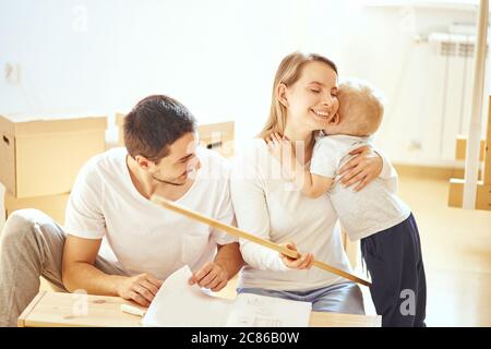 family with little boy assembling furniture at home, mother and son hugging after finishing assemble Stock Photo