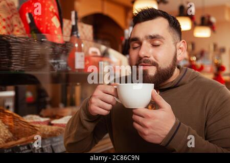 Happy bearded young man enjoying smell of fresh coffee, having breakfast at the cafe, copy space Stock Photo