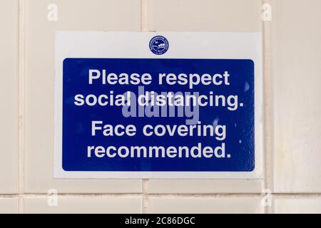 Notice on the wall in a public toilet to Please respect social distancing, face covering recommended, during 2020 coronavirus covid-19 pandemic Stock Photo