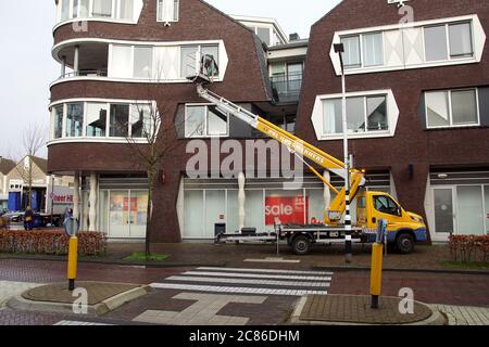Window cleaner in a bucket of a telescopic boom lift on a truck cleans the windows of an apartment. Netherlands, January Stock Photo