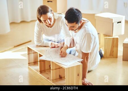 couple reads instructions for Assembly of furniture in new house with moving boxes on background Stock Photo