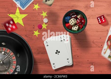 China casino theme. Aces in poker game, cards and chips on red table with national flag background. Gambling and betting. Stock Photo