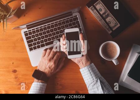 Smartphone mock up overhead shot, businessman holding mobile phone with blank screen over office desk and laptop computer Stock Photo