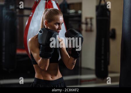 young female boxer in gloves standing in defense pose and looking focused a side Stock Photo