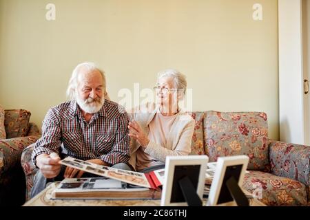 Pleasant-looking old pensioners couple watching old pictures at family album, being proud and happy that they were able to save the marriage and bring Stock Photo